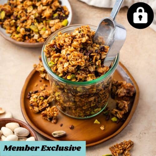 A glass jar of granola sitting on a small wooden plate.