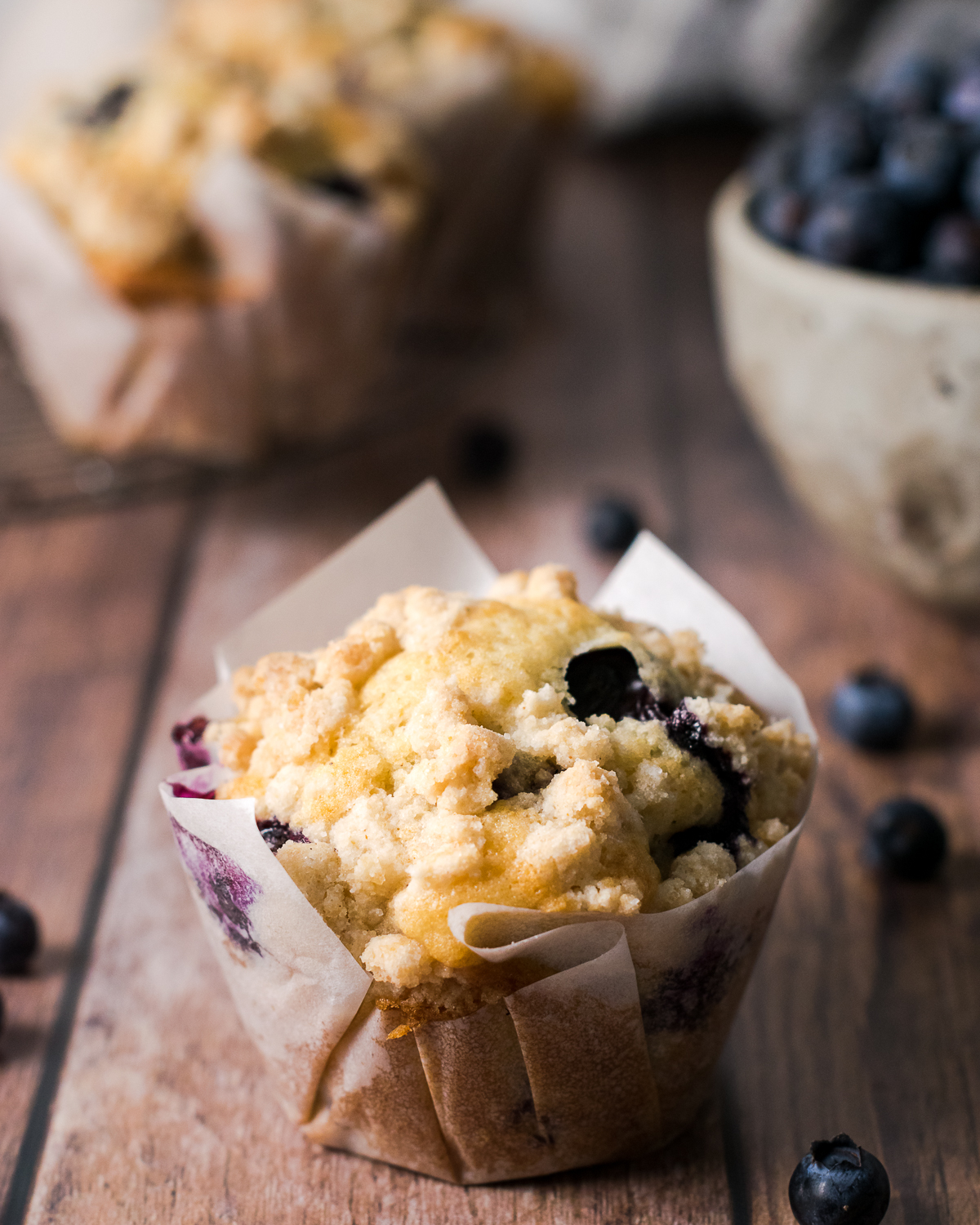 A single gluten free blueberry muffin in a paper wrapper sitting on a wood table.