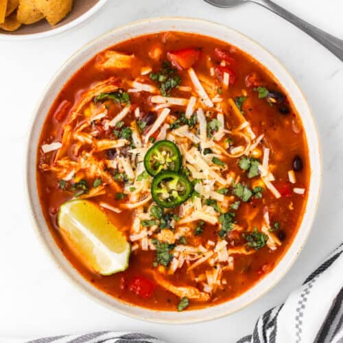 A bowl of chicken taco soup topped with shredded cheese and sliced jalapenos.