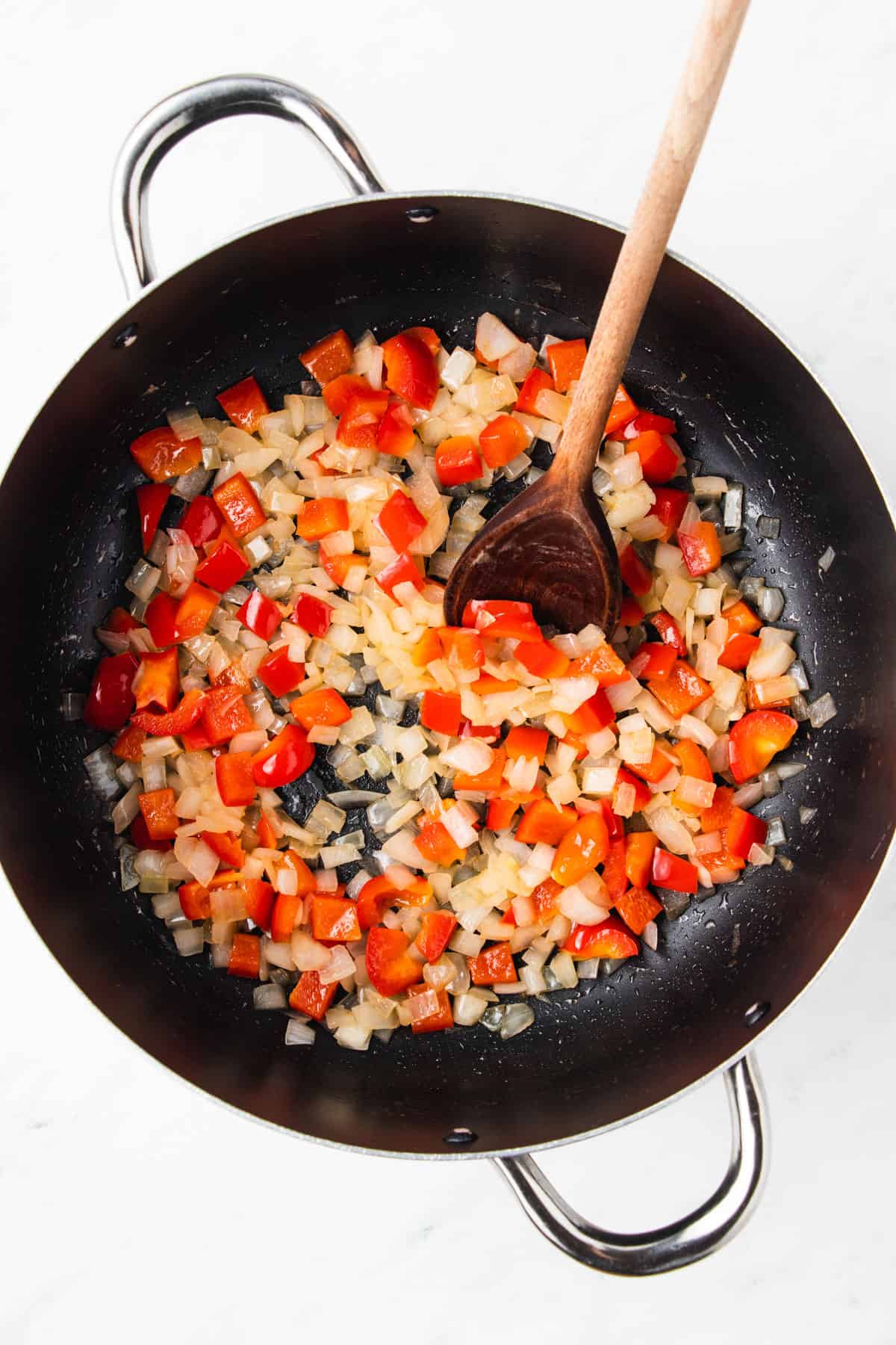 Diced red bell pepper and onions being sauteed in a large pot.
