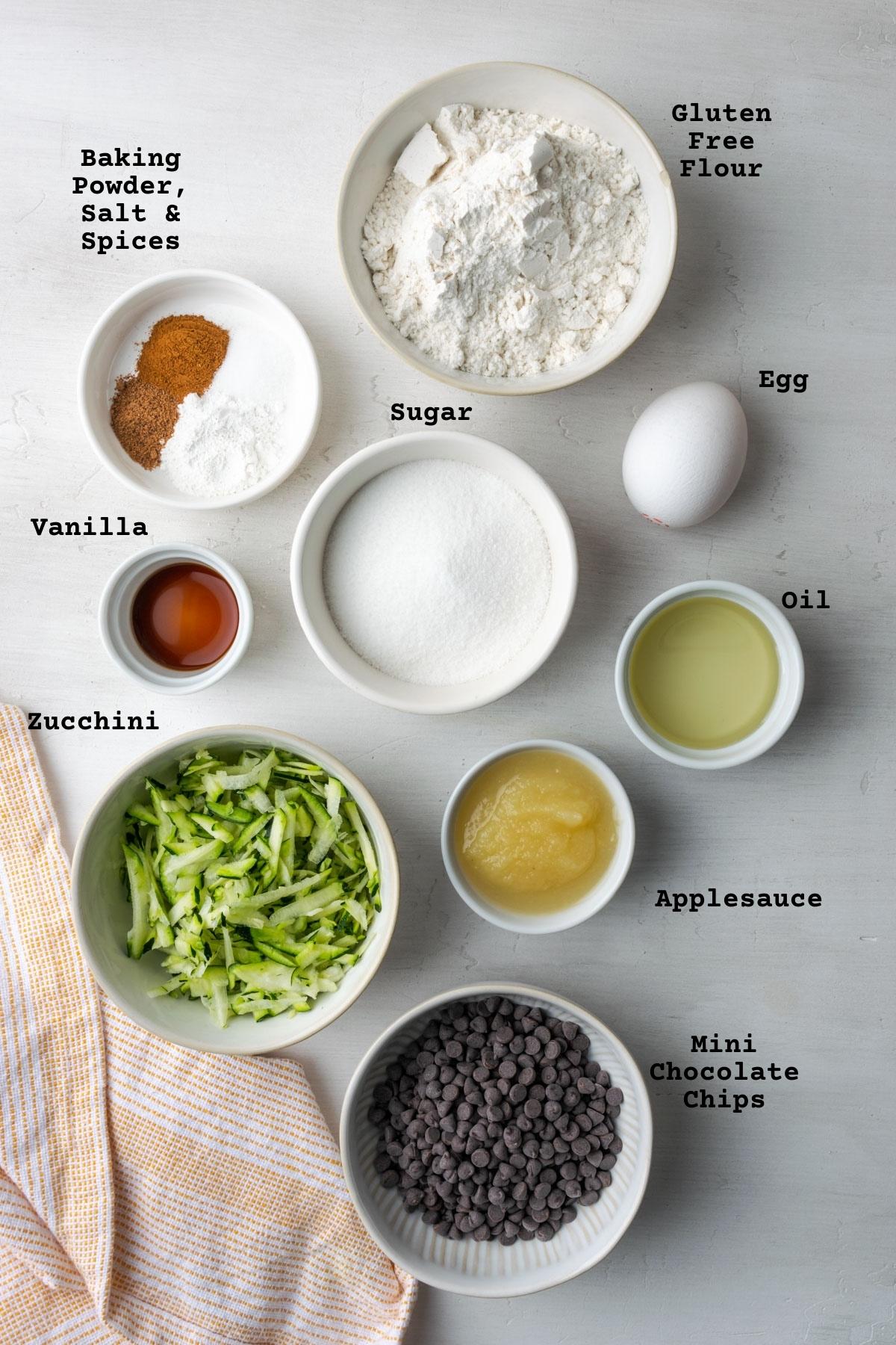 Ingredients for gluten free zucchini chocolate chip muffins on a white table.