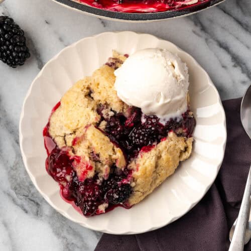 A serving of gluten free blackberry cobbler with a scoop of ice cream on a small dessert plate.
