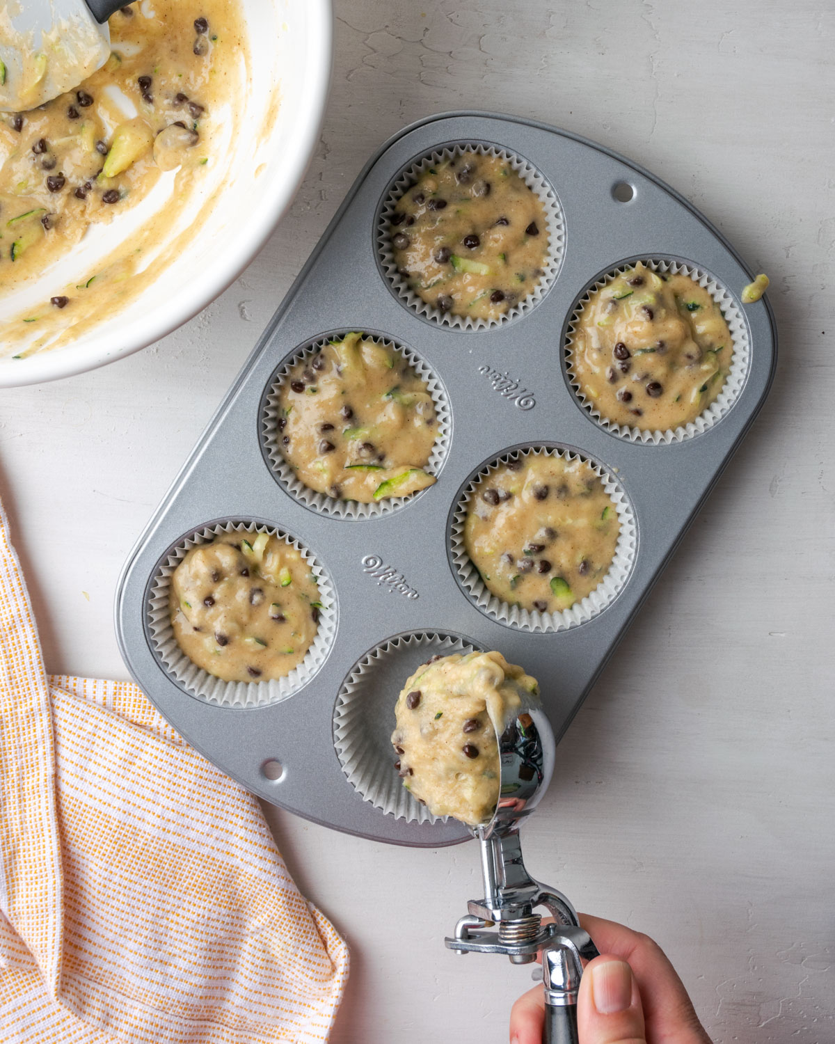 Zucchini muffin batter being scooped into a muffin tin.