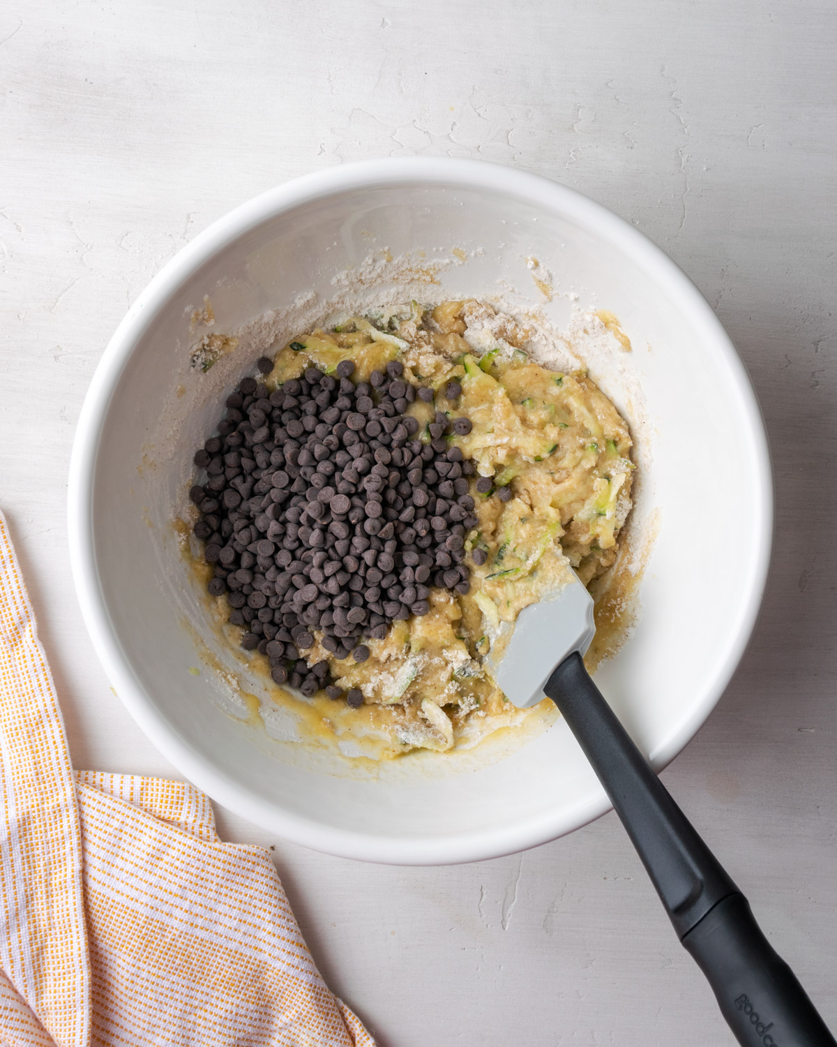 Mini chocolate chips being folded into the partially mixed zucchini muffin batter.