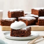 A slice of chocolate potato cake topped with whipped cream and served on a white plate.