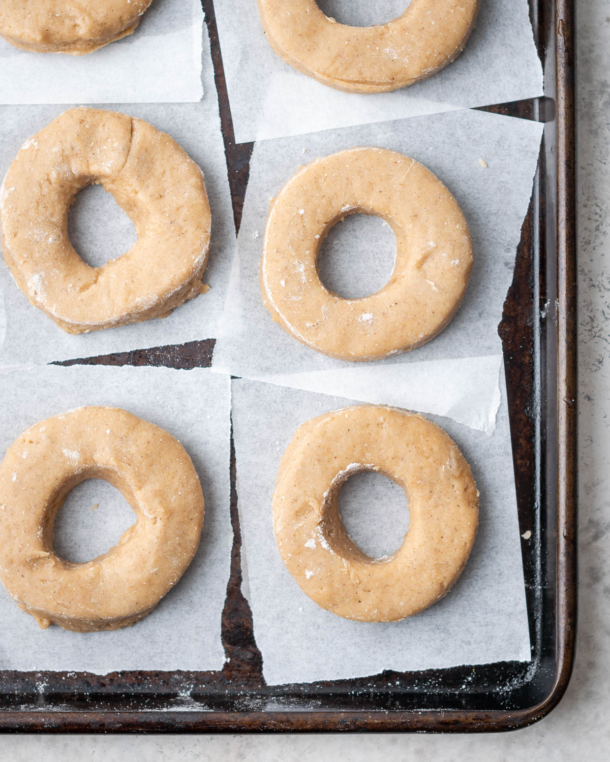 Cut out gluten free apple cider donuts laying on a baking sheet. 