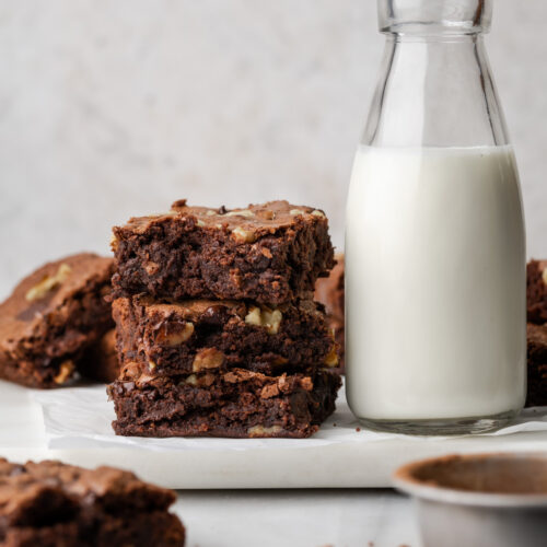 A stack of brownies next to a jar of milk.
