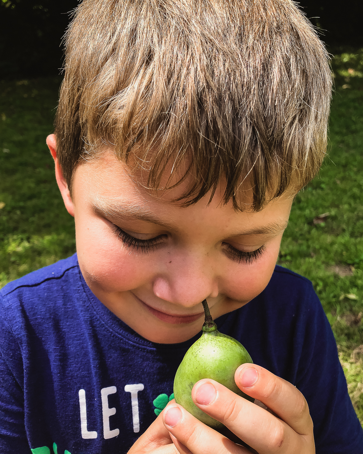 Boy holding a paw paw fruit near his nose.