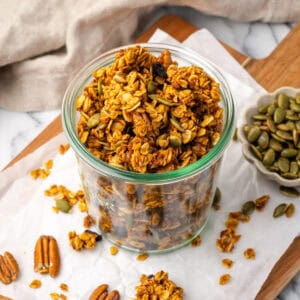 A jar of pumpkin seed granola sitting next to a small dish of pumpkin seeds on a wood tray.