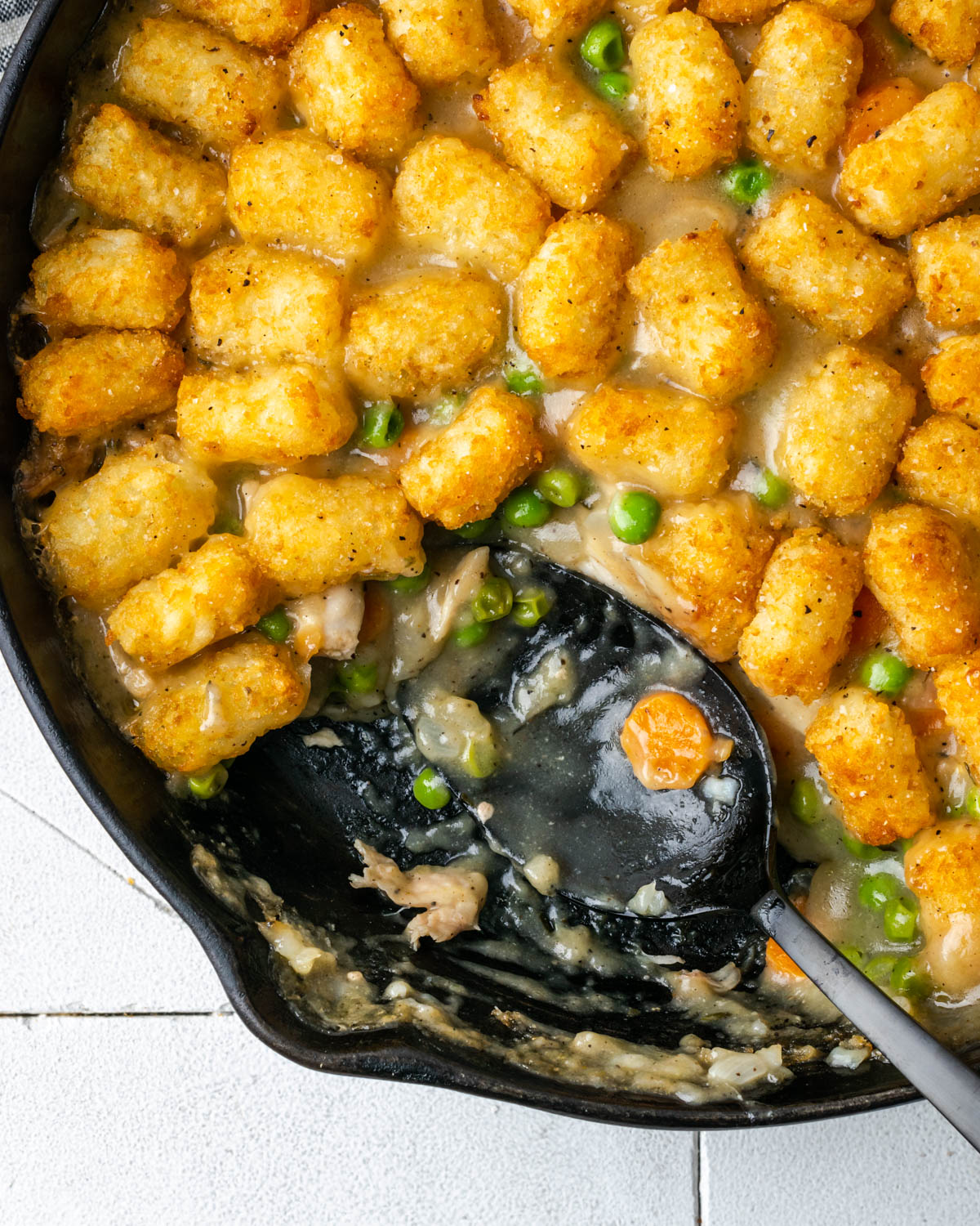 A chicken pot pie casserole with tater tots in a cast iron skillet.
