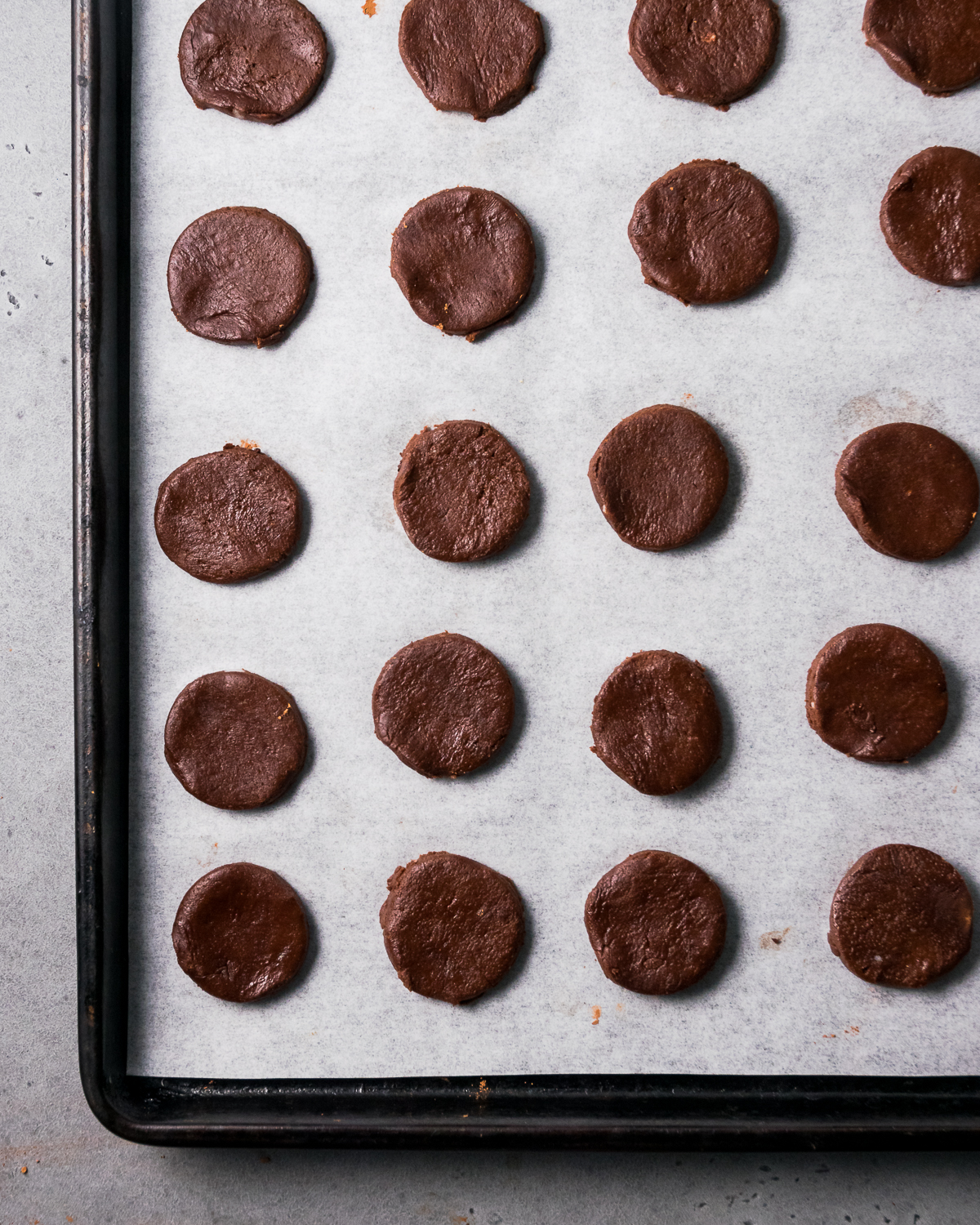 Small unbaked thin mint cookies on a lined baking sheet.
