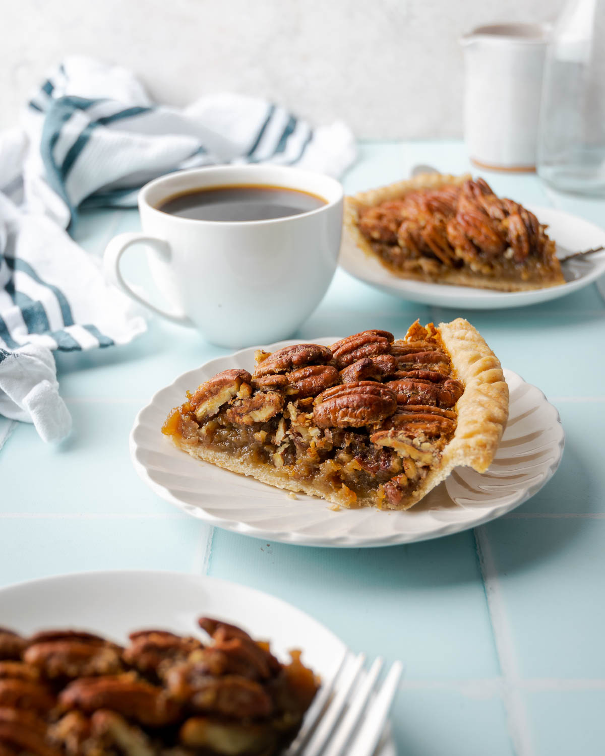 A slice of pecan pie on a white plate served with a cup of coffee.