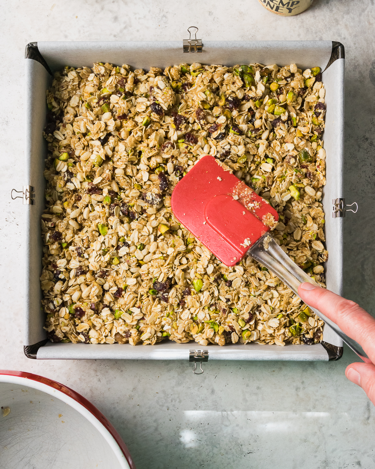 Unbaked granola being spread into a tight even layer in a square pan.