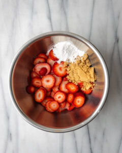 Strawberries, sugar and cornstarch in a metal bowl.