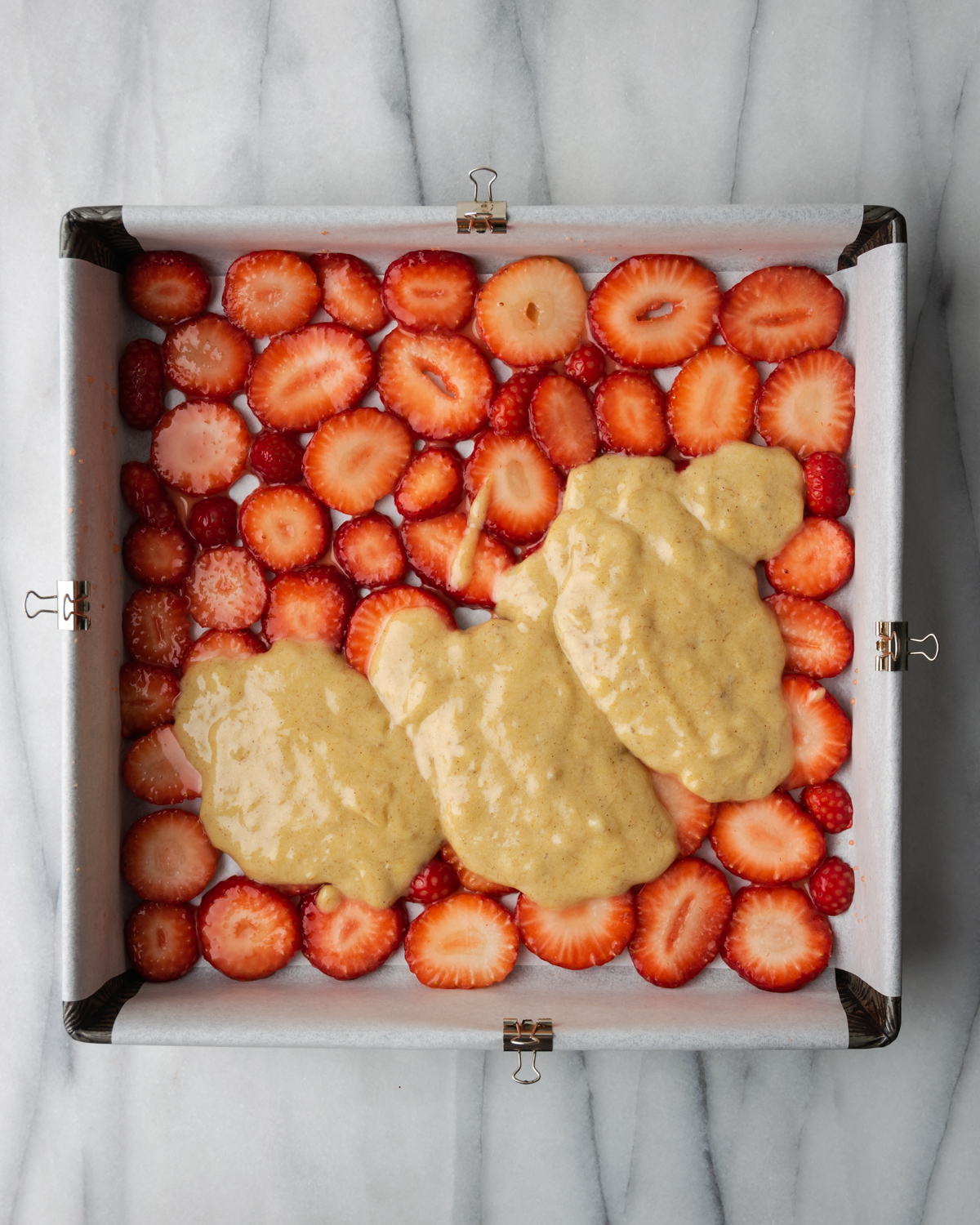 Batter being spooned over strawberry layer.