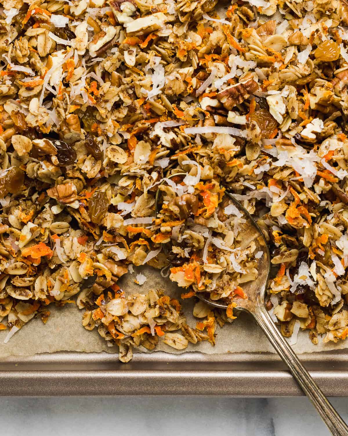 Carrot cake granola being spooned off a baking sheet.