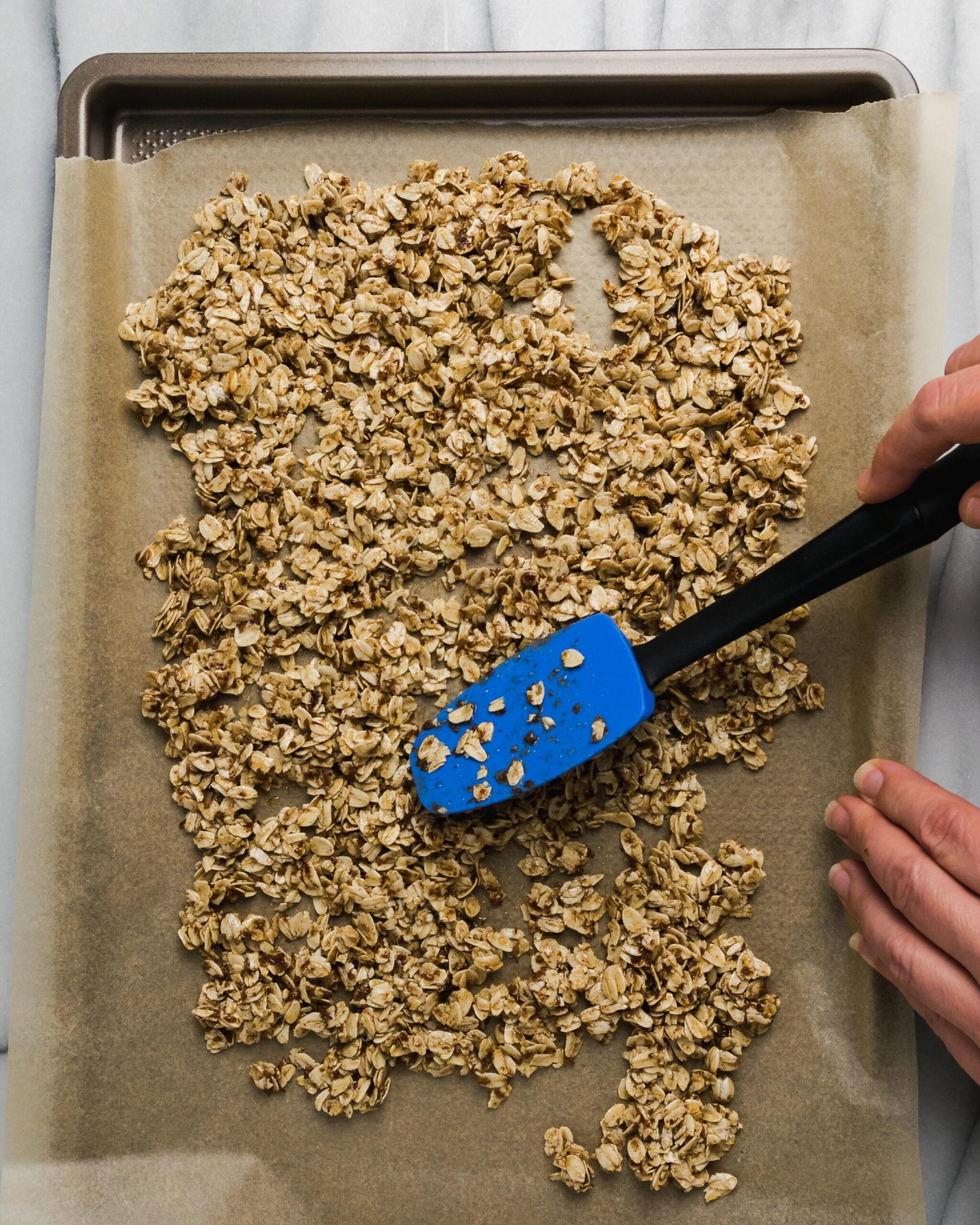 Granola being spread out on baking sheet.