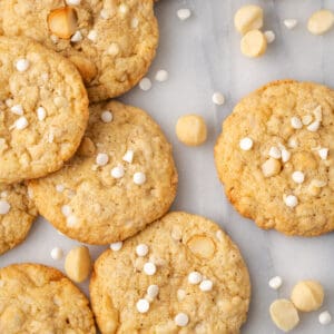 A batch of gluten free white chocolate macadamia nut cookies scattered on a white table.