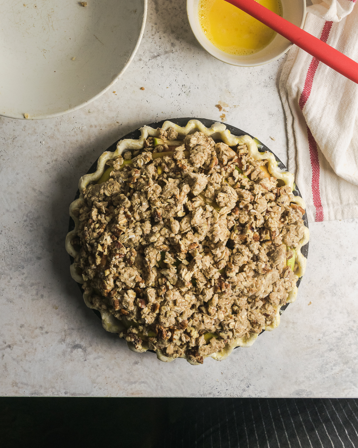 Unbaked apple pie with crumble topping on a white table.