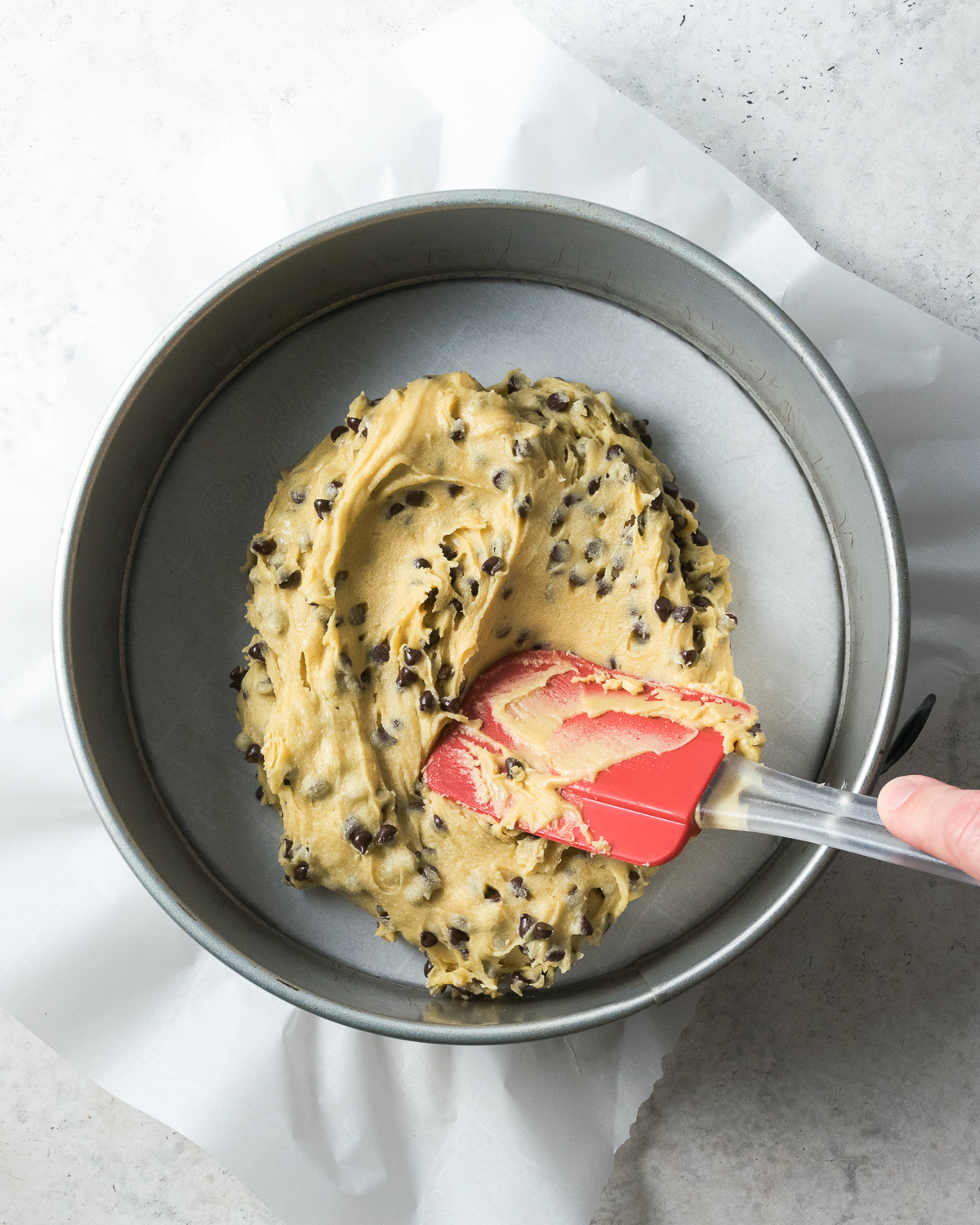 Cookie dough being spread into a large pan to make a cookie cake.