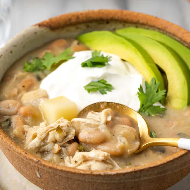 A bowl of white chicken chili topped with sour cream and sliced avocado.