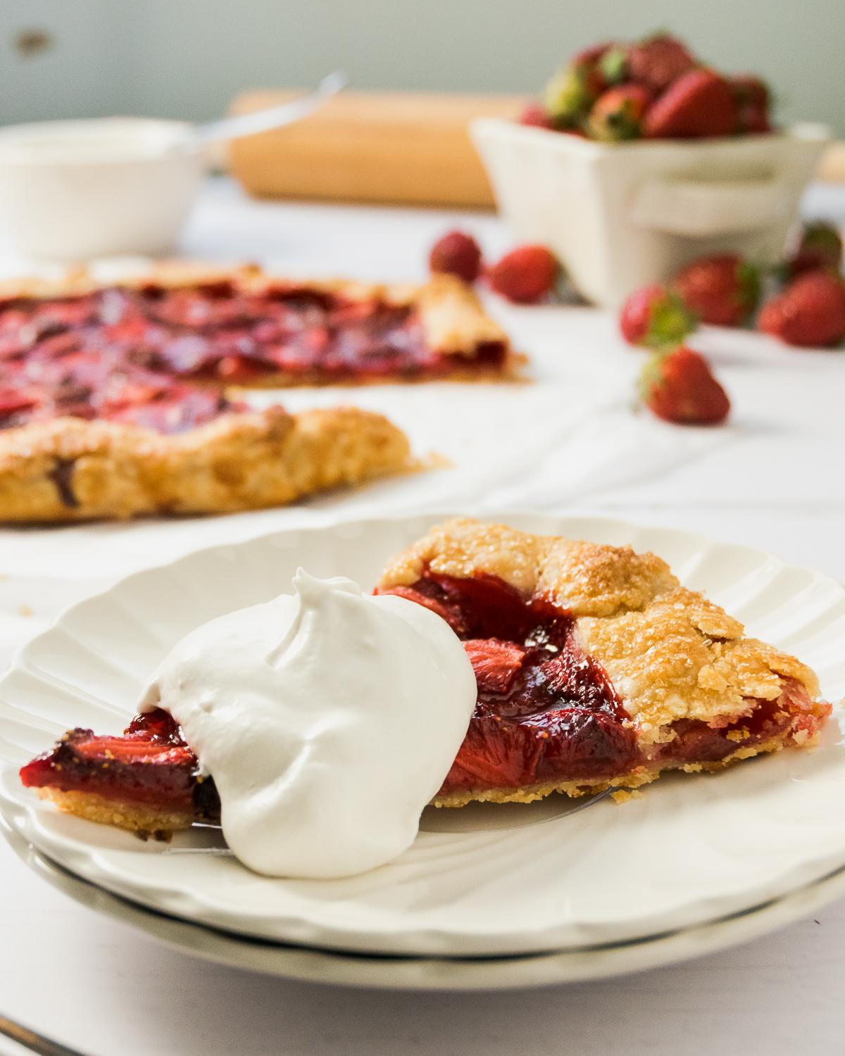 A slice of strawberry galette on a plate topped with whipped cream.
