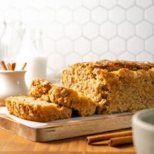 A loaf of maple banana bread sliced and sitting on a wooden cutting board.