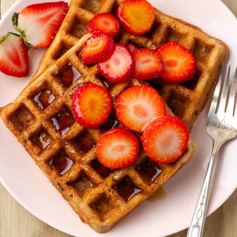 Two strawberry waffles topped with syrup and slices of fresh strawberries.