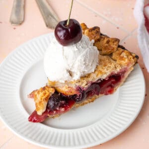 A slice of apple cherry pie topped with vanilla ice cream.