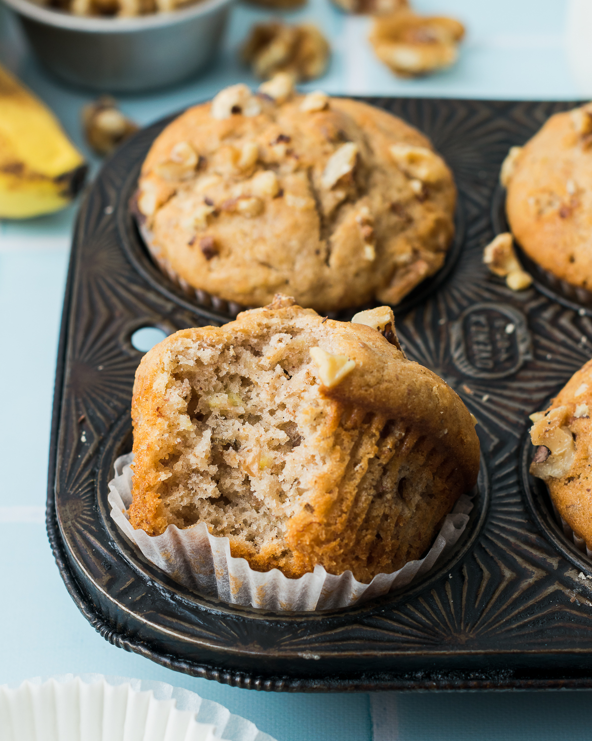 Freshly baked gluten free banana muffins sitting in a muffin tin on a blue tile table.