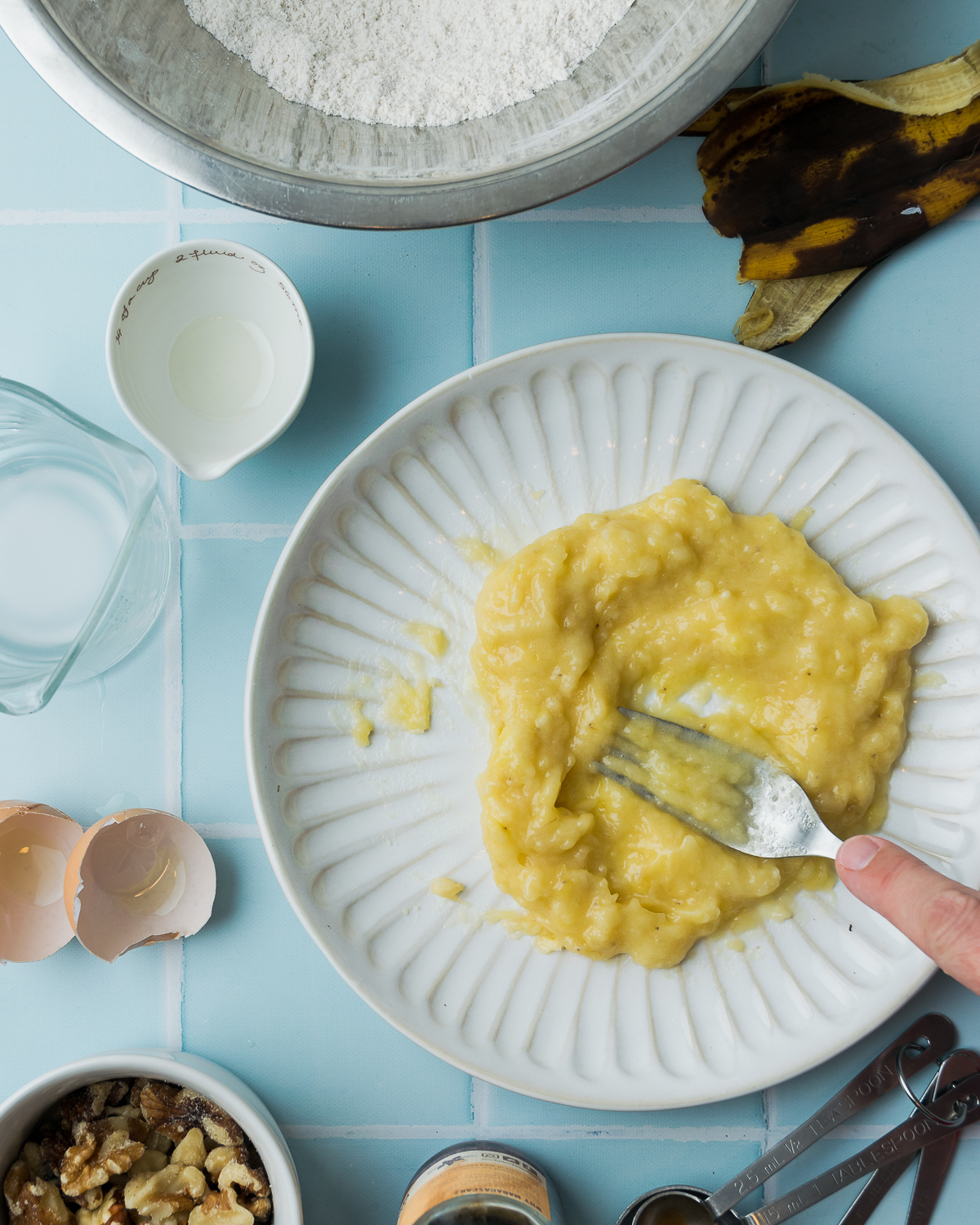 A banana being mashed with a fork on a white plate.