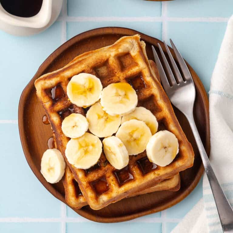 A plate of gluten free banana waffles topped with slices of banana and maple syrup.