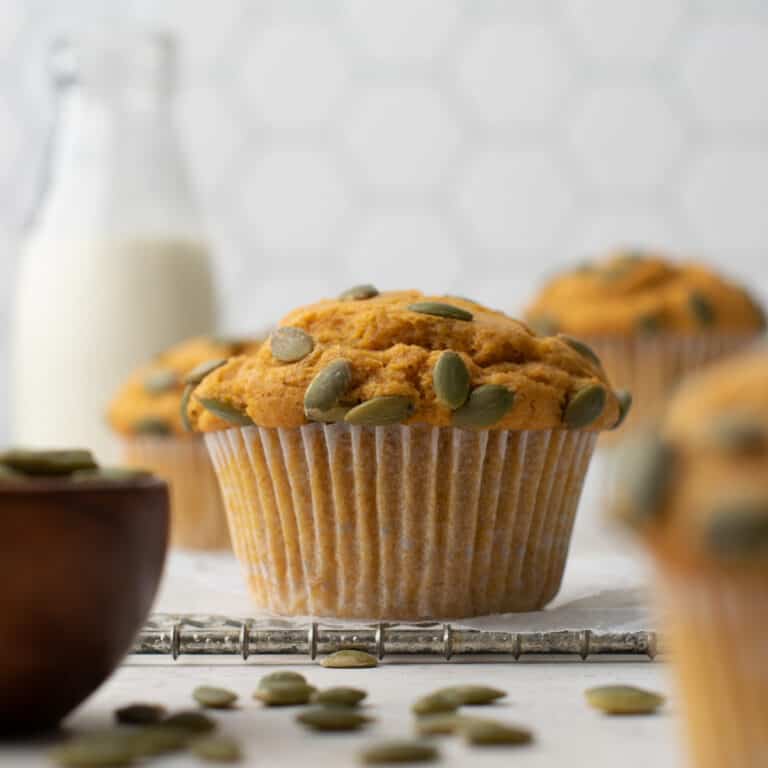 A gluten free pumpkin muffin topped with pumpkin seeds and sitting on a metal cooling rack.