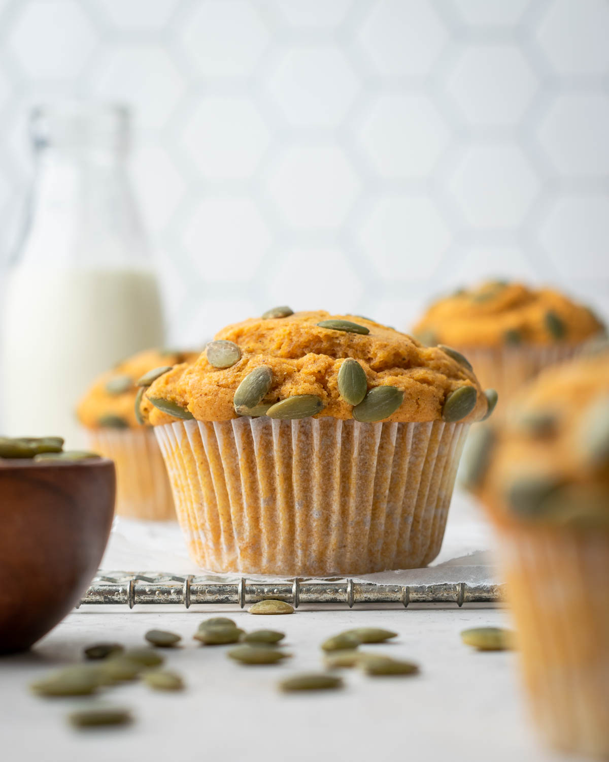 A pumpkin muffin topped with pumpkin seeds on a white table.