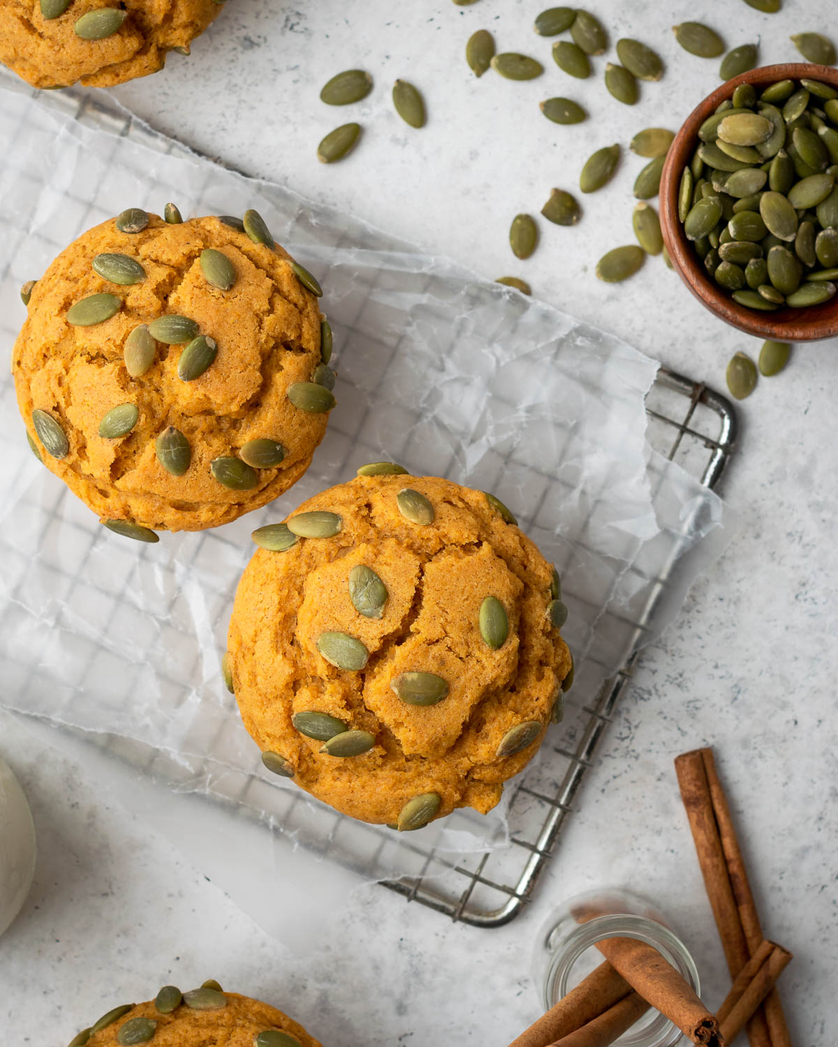 Two gluten free pumpkin muffins sitting on a metal cooling rack.