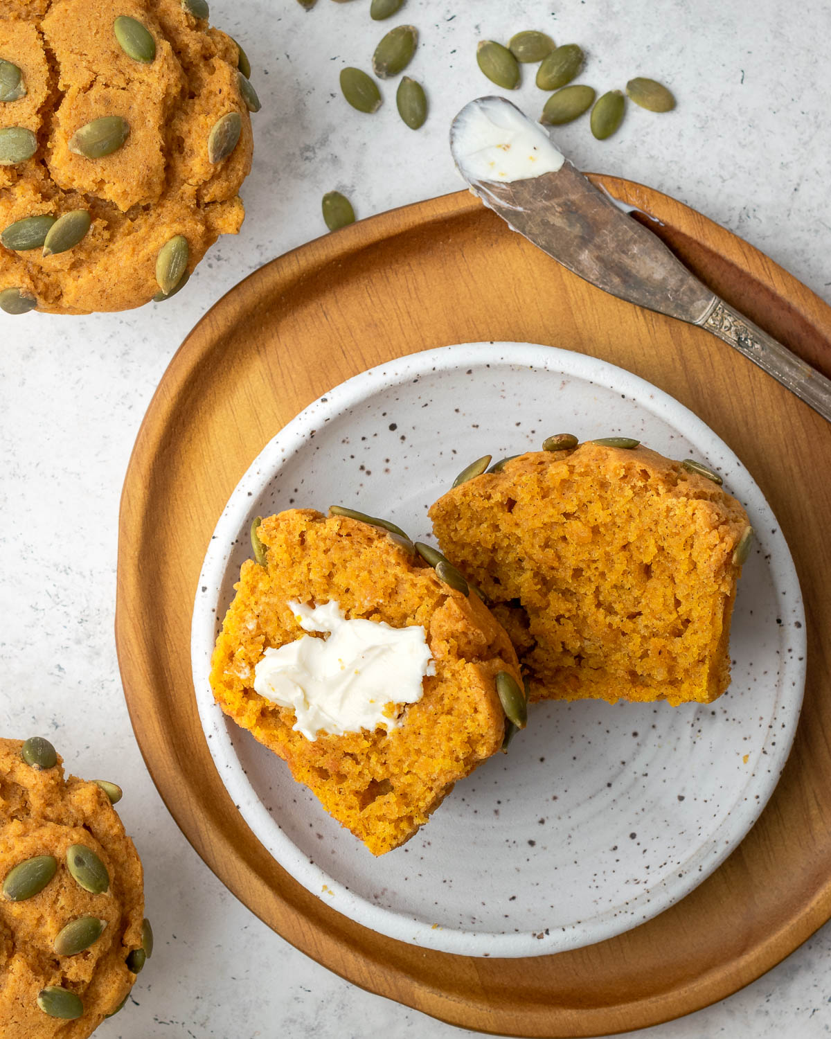 A pumpkin muffin sliced open on a plate and spread with butter.