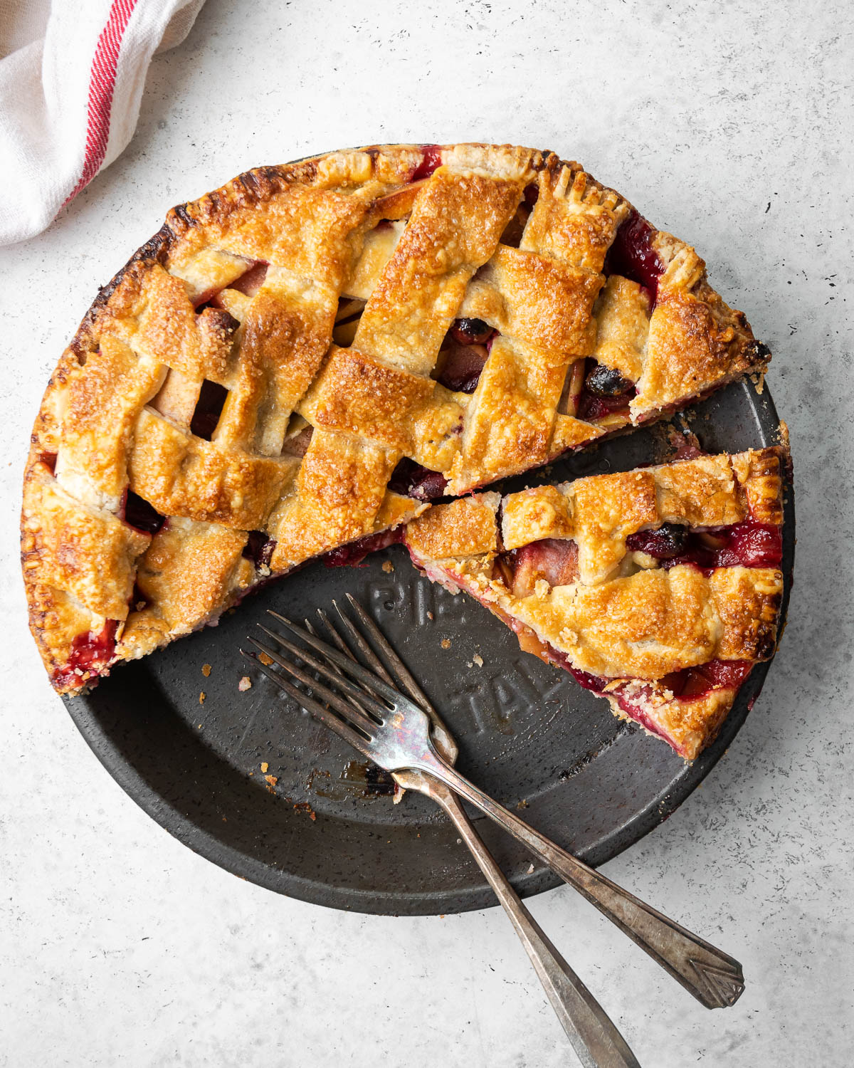 Overhead view of a cut cranberry apple pie on a white table.