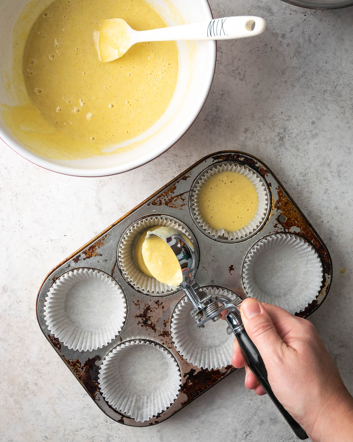 Corn muffin batter being portioned into a muffin pan.