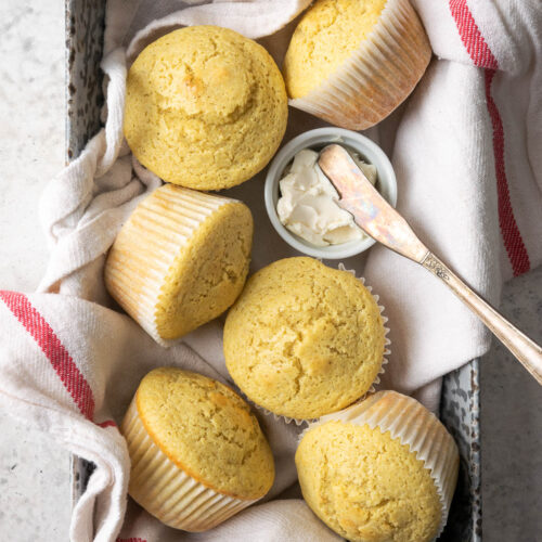 A basket of gluten free corn muffins on a white table.