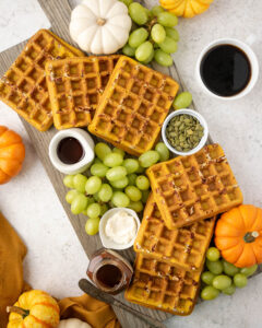 Pumpkin waffles on a waffle board with grapes and spreads.