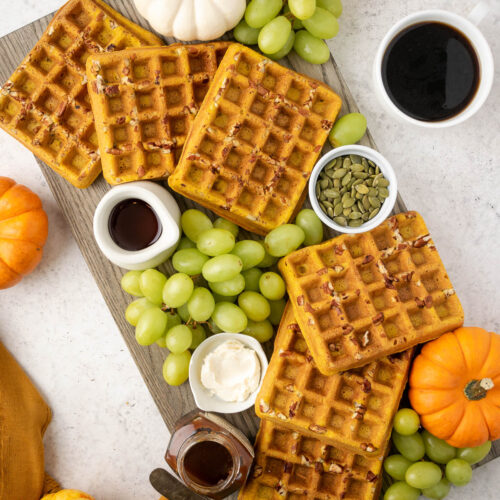 Pumpkin waffles on a waffle board with grapes and spreads.