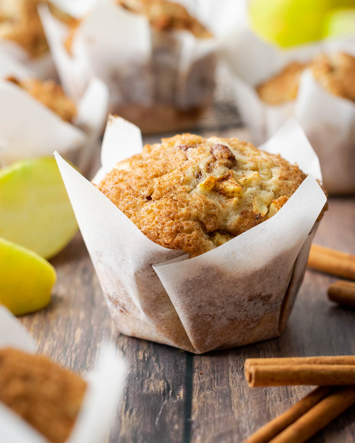 An apple muffin sprinkled with sugar and cinnamon sitting on a wooden table.