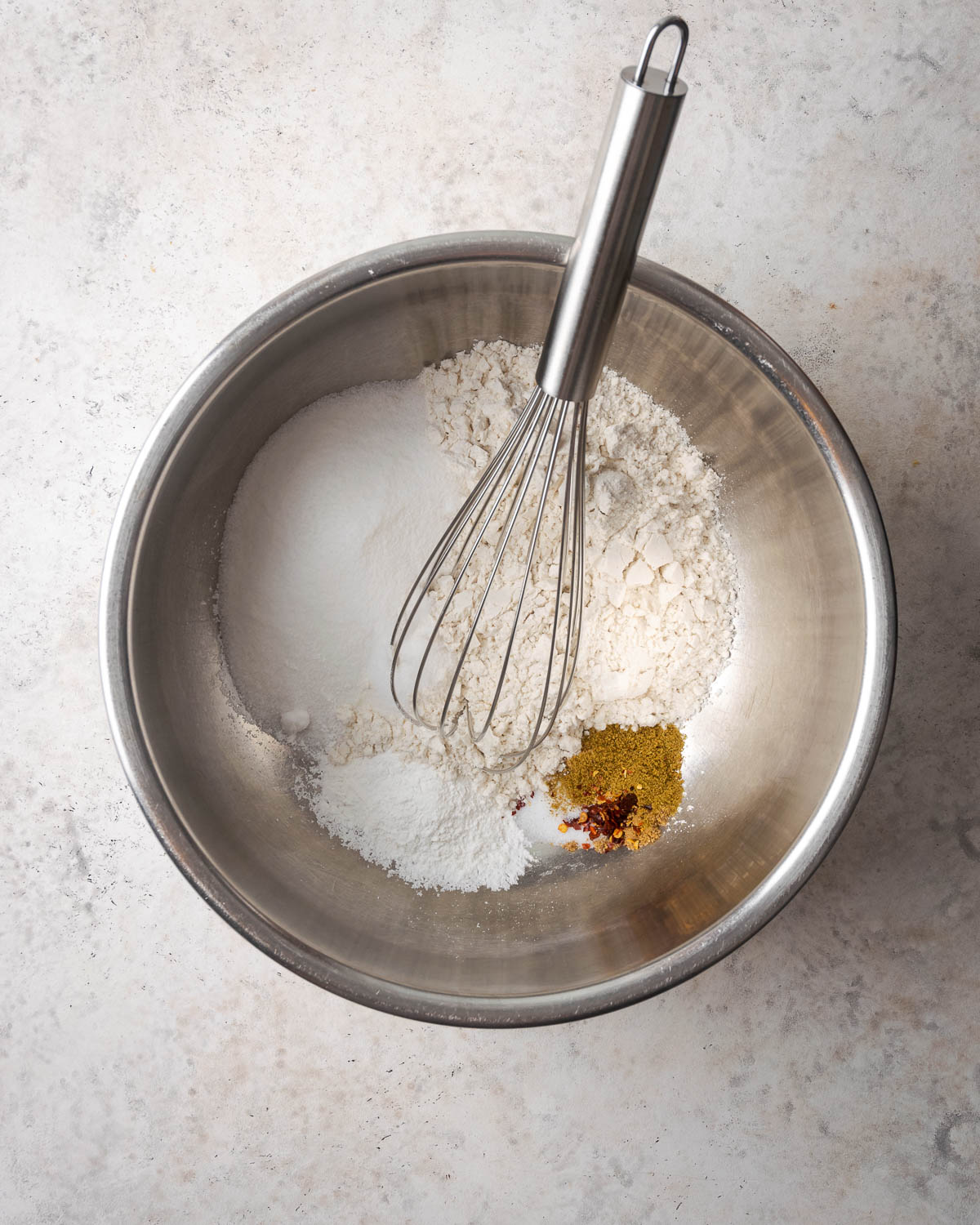 Gluten free flour, sugar, baking powder, salt and spices being whisked together in a metal mixing bowl.