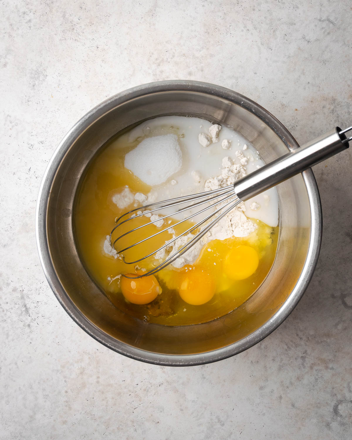 Eggs and milk added to the dry ingredients in a metal mixing bowl.