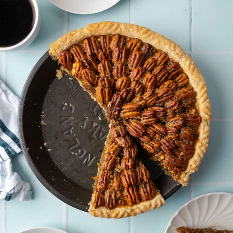 A sliced pecan pie on a light blue table.