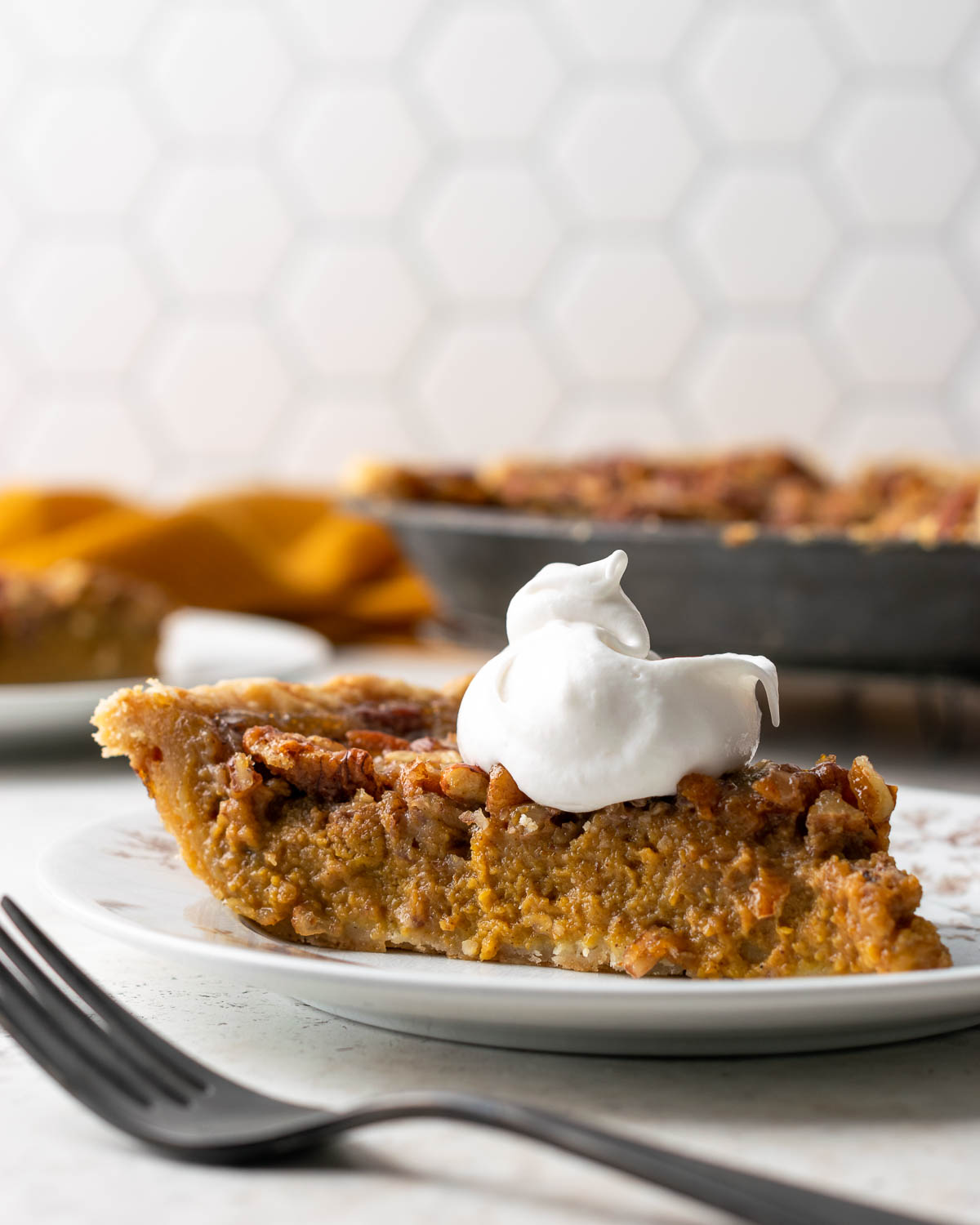 A slice of pumpkin pecan pie topped with whipped cream.