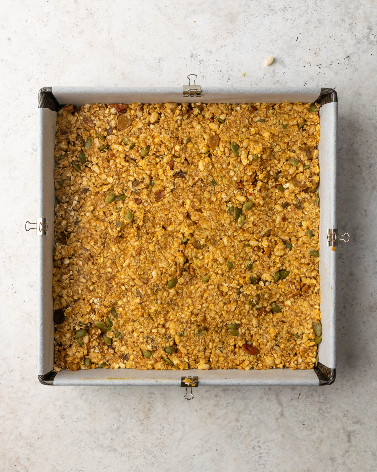 Unbaked pumpkin granola bars in a square baking tin.