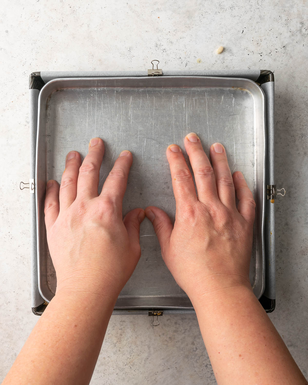 A smaller baking pan being pressed into the square tin to flatten the granola.