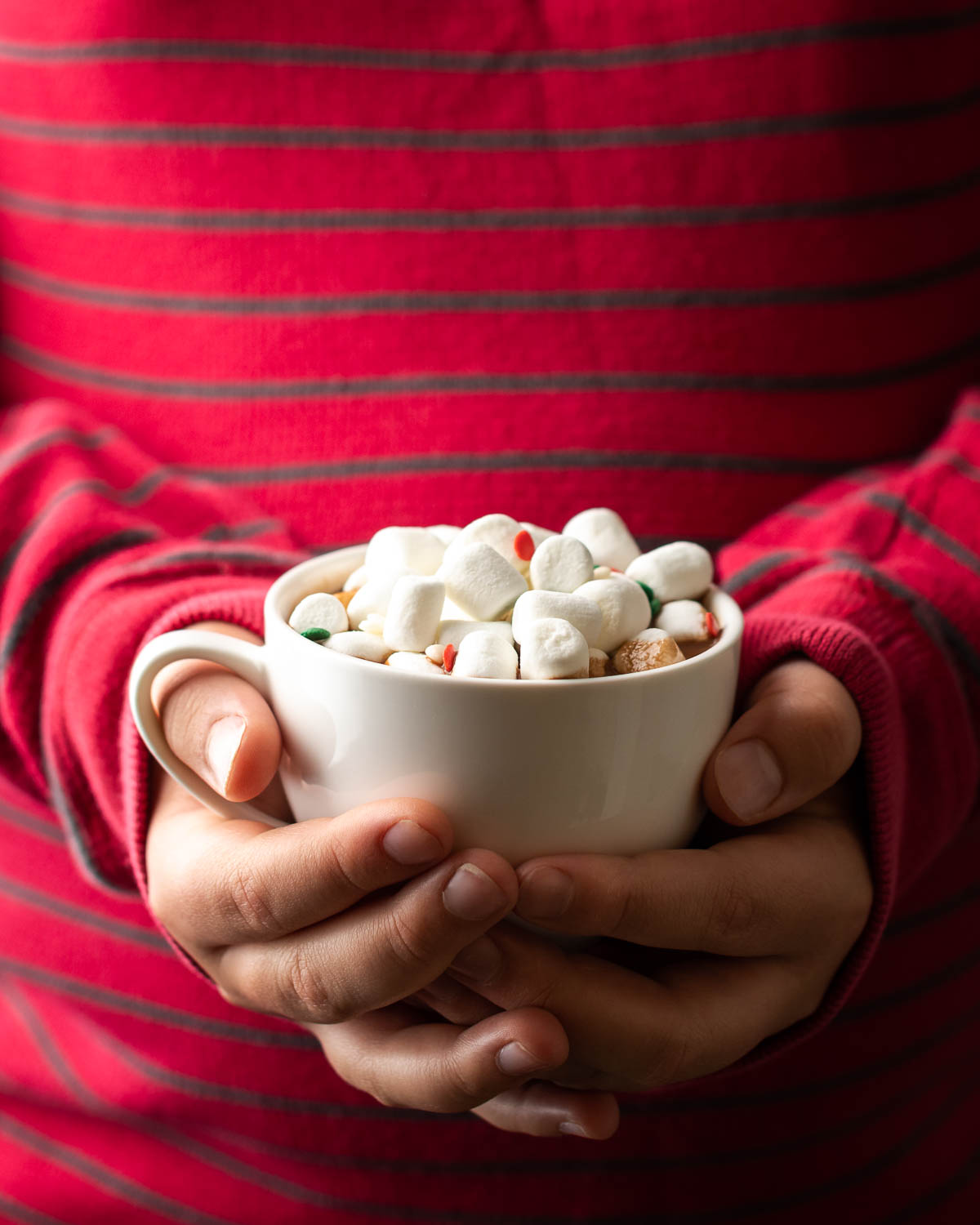 Child's hands holding a cup of hot chocolate with marshmallows.
