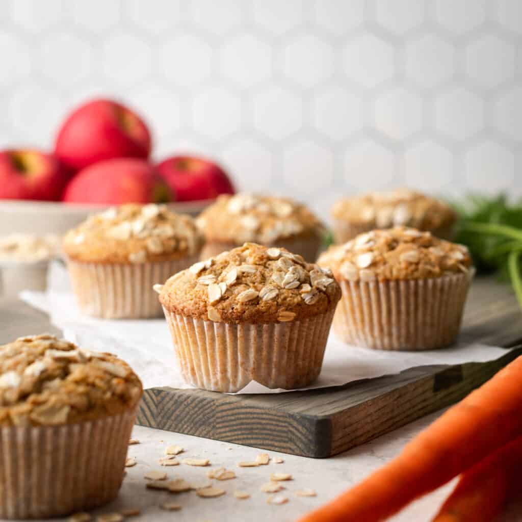 Applesauce carrot muffins sitting on a wooden cutting board.